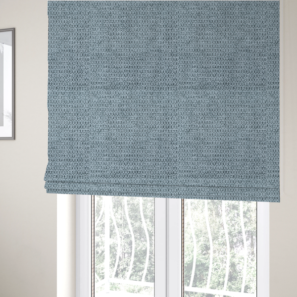 The fabric used to create these Roman blinds is a textured fabric in a light steel or airy powder blue. This material features a dense, rhythmic weave with a tactile, honeycomb-like surface. The colour is a cool, soft frost blue, achieved by interlacing pale blue threads with darker grey base fibres, resulting in a weathered, multidimensional look that feels light yet substantial.