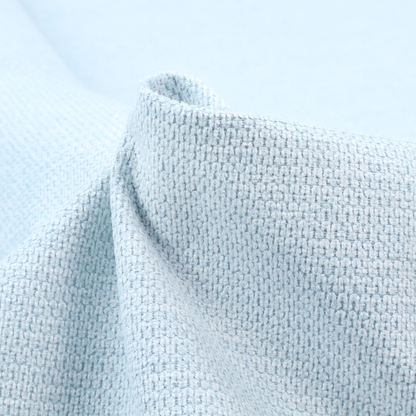 A textured fabric in a pale sky blue. This material features a dense, rhythmic weave with a delicate honeycomb-like surface. The colour is a bright, airy pastel blue, achieved by interlacing soft blue threads with a crisp white base, resulting in a luminous, clean appearance that emphasizes the fabric's tactile grid.