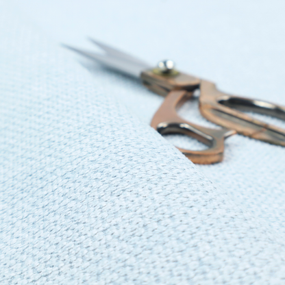 A textured fabric in a pale sky blue. This material features a dense, rhythmic weave with a delicate honeycomb-like surface. The colour is a bright, airy pastel blue, achieved by interlacing soft blue threads with a crisp white base, resulting in a luminous, clean appearance that emphasizes the fabric's tactile grid.