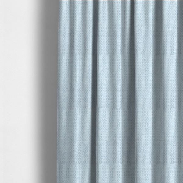 The fabric used to create these made-to-measure curtains is a textured fabric in a pale sky blue. This material features a dense, rhythmic weave with a delicate honeycomb-like surface. The colour is a bright, airy pastel blue, achieved by interlacing soft blue threads with a crisp white base, resulting in a luminous, clean appearance that emphasizes the fabric's tactile grid.