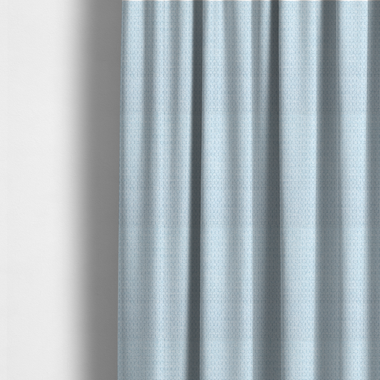 The fabric used to create these made-to-measure curtains is a textured fabric in a pale sky blue. This material features a dense, rhythmic weave with a delicate honeycomb-like surface. The colour is a bright, airy pastel blue, achieved by interlacing soft blue threads with a crisp white base, resulting in a luminous, clean appearance that emphasizes the fabric's tactile grid.