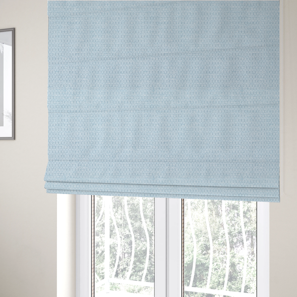 The fabric used to create these Roman blinds is a textured fabric in a pale sky blue. This material features a dense, rhythmic weave with a delicate honeycomb-like surface. The colour is a bright, airy pastel blue, achieved by interlacing soft blue threads with a crisp white base, resulting in a luminous, clean appearance that emphasizes the fabric's tactile grid.