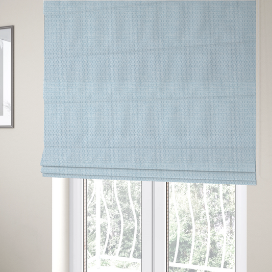 The fabric used to create these Roman blinds is a textured fabric in a pale sky blue. This material features a dense, rhythmic weave with a delicate honeycomb-like surface. The colour is a bright, airy pastel blue, achieved by interlacing soft blue threads with a crisp white base, resulting in a luminous, clean appearance that emphasizes the fabric's tactile grid.