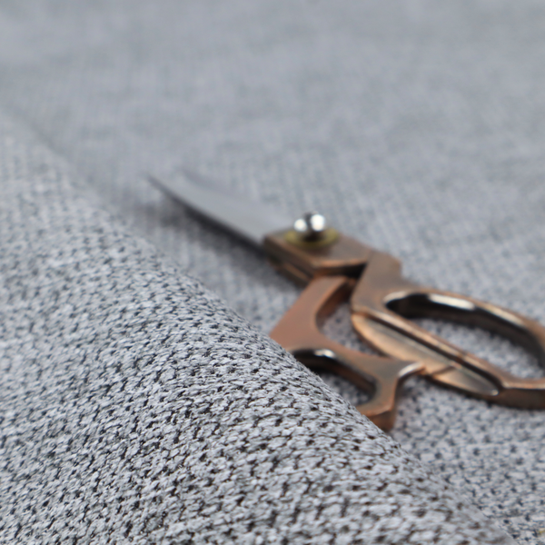 A textured fabric in a classic charcoal or weathered grey. The material features a dense, rhythmic weave with a tactile, pebbled surface. The colour is a sophisticated mid-grey, achieved by interlacing silver-grey threads with darker black base fibres, creating a high-contrast, multidimensional look that feels balanced and durable.