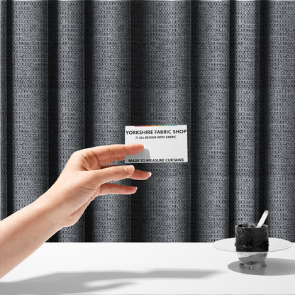 The fabric used to create these made-to-measure curtains is a textured fabric in a classic charcoal or weathered grey. The material features a dense, rhythmic weave with a tactile, pebbled surface. The colour is a sophisticated mid-grey, achieved by interlacing silver-grey threads with darker black base fibres, creating a high-contrast, multidimensional look that feels balanced and durable.