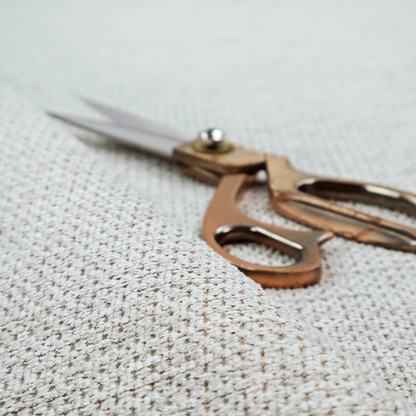 A textured fabric in light greige or pale oatmeal. The material features a dense, rhythmic honeycomb weave. The colour is achieved by interlacing light cream threads with cool grey base fibres, creating a neutral, stony appearance with a soft, pebbled tactile surface.