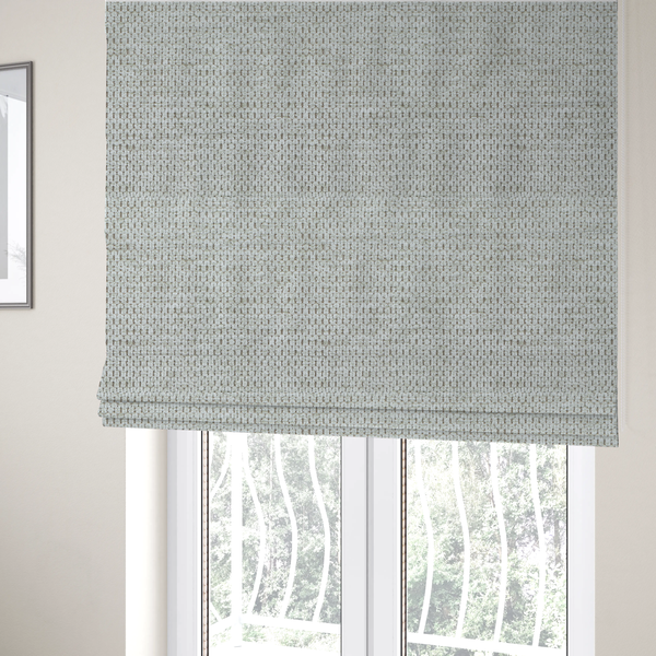 The fabric used to create these Roman blinds is a textured fabric in light greige or pale oatmeal. The material features a dense, rhythmic honeycomb weave. The colour is achieved by interlacing light cream threads with cool grey base fibres, creating a neutral, stony appearance with a soft, pebbled tactile surface.