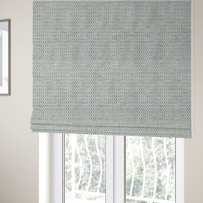 The fabric used to create these Roman blinds is a textured fabric in light greige or pale oatmeal. The material features a dense, rhythmic honeycomb weave. The colour is achieved by interlacing light cream threads with cool grey base fibres, creating a neutral, stony appearance with a soft, pebbled tactile surface.