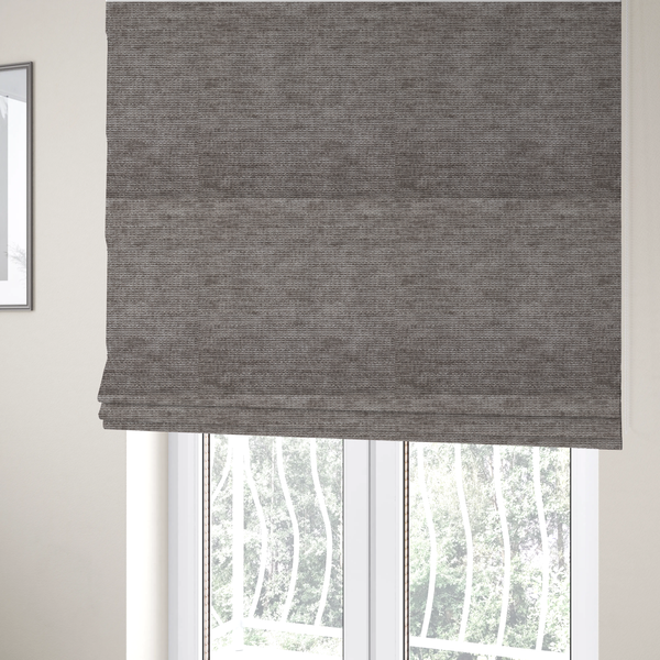 The fabric used to create these Roman blinds is a taupe or ash brown fabric with a dense, horizontal ribbed texture. The material features a soft, velvety pile that creates subtle light-catching highlights and shadows across the linear weave.