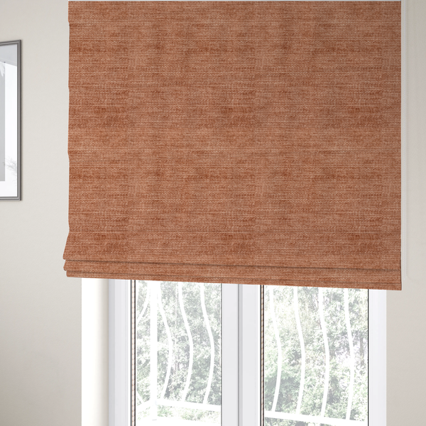The fabric used to create these Roman blinds is a burnt orange fabric with a dense, horizontal corded texture. The weave has a soft, plush pile similar to corduroy, creating a rich tonal depth with warm highlights and subtle shadows across the linear pattern.