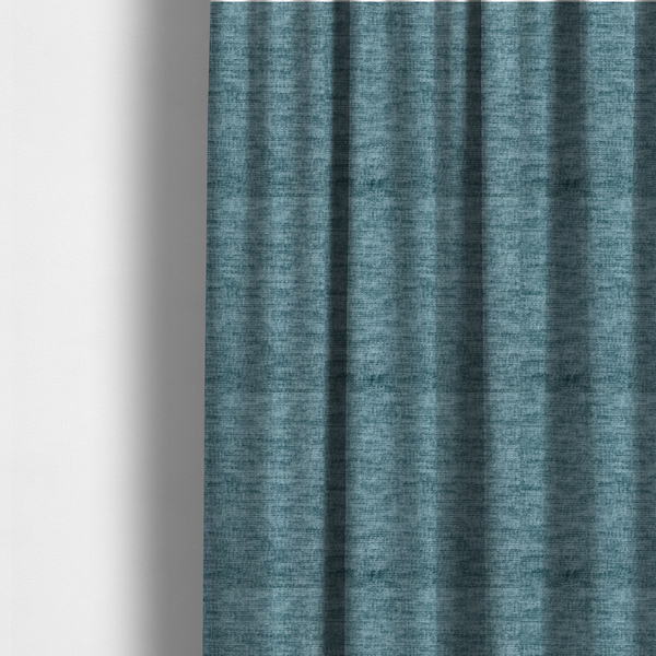 The fabric used to create these made-to-measure curtains is a teal or dusty blue fabric with a soft, weathered texture. The weave features a subtle horizontal grain with a plush, multi-tonal pile that blends shades of slate and ocean blue for a rich, tactile appearance.
