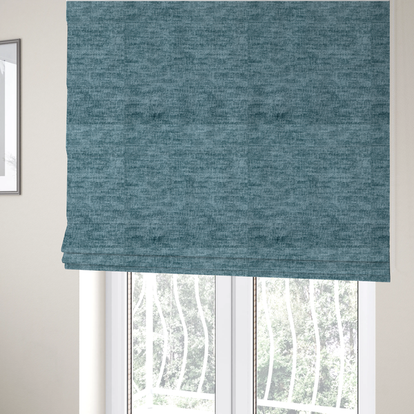 The fabric used to create these Roman blinds is a teal or dusty blue fabric with a soft, weathered texture. The weave features a subtle horizontal grain with a plush, multi-tonal pile that blends shades of slate and ocean blue for a rich, tactile appearance.