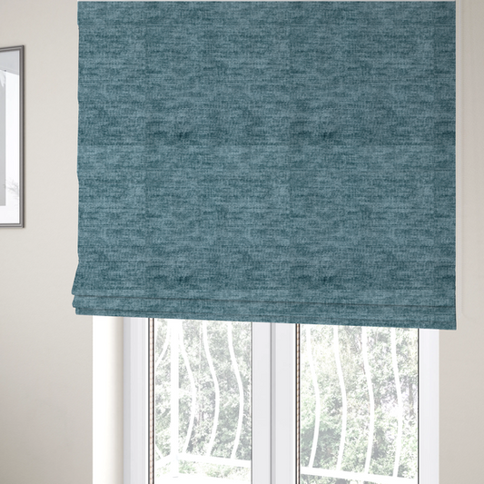 The fabric used to create these Roman blinds is a teal or dusty blue fabric with a soft, weathered texture. The weave features a subtle horizontal grain with a plush, multi-tonal pile that blends shades of slate and ocean blue for a rich, tactile appearance.