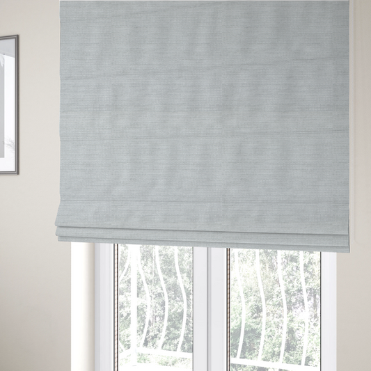The fabric used to create these Roman blinds is a cool, silver-white fabric with a soft, uniform horizontal ribbed texture. The material features a plush, chenille-like pile that provides a subtle, velvety sheen, catching the light across the fine linear ridges for a clean and modern look.