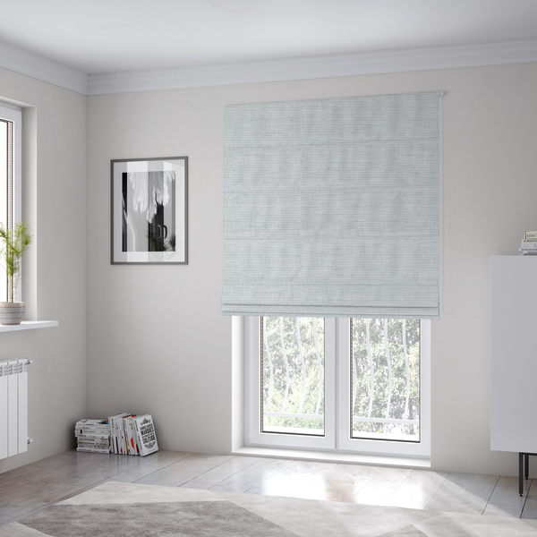 The fabric used to create these Roman blinds is a cool, silver-white fabric with a soft, uniform horizontal ribbed texture. The material features a plush, chenille-like pile that provides a subtle, velvety sheen, catching the light across the fine linear ridges for a clean and modern look.