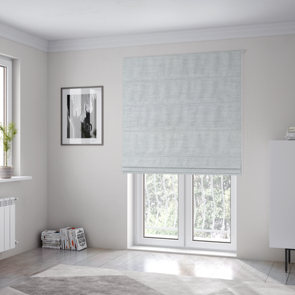 The fabric used to create these Roman blinds is a cool, silver-white fabric with a soft, uniform horizontal ribbed texture. The material features a plush, chenille-like pile that provides a subtle, velvety sheen, catching the light across the fine linear ridges for a clean and modern look.