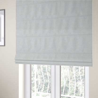 The fabric used to create these Roman blinds is a light-coloured, woven contract fabric. The material features a fine, grid-like texture resembling a mix of linen and grass cloth in a neutral off-white or pale pearl tone. The weave creates a subtle, matte geometric pattern with delicate shadows that give the surface a tactile, three-dimensional appearance.