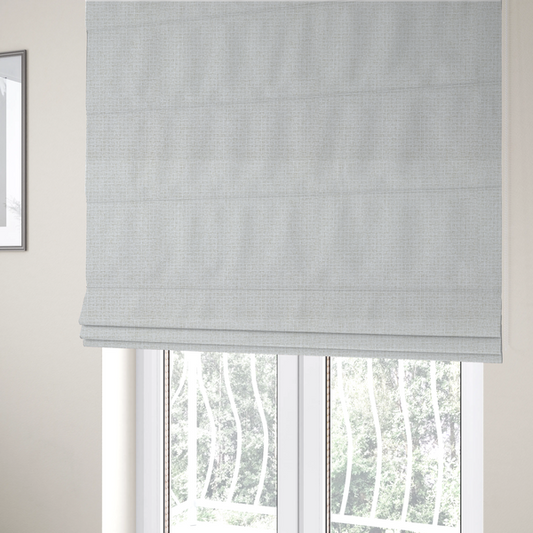 The fabric used to create these Roman blinds is a light-coloured, woven contract fabric. The material features a fine, grid-like texture resembling a mix of linen and grass cloth in a neutral off-white or pale pearl tone. The weave creates a subtle, matte geometric pattern with delicate shadows that give the surface a tactile, three-dimensional appearance.