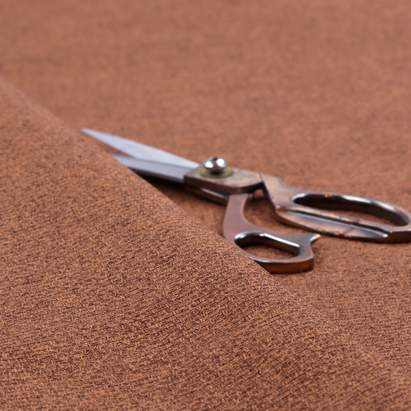 An upholstery fabric in a warm terracotta or burnt orange shade. The textile features a multi-tonal basket weave with interlacing copper and dark brown threads, creating a rich, textured linen-look surface with an earthy, matte finish.
