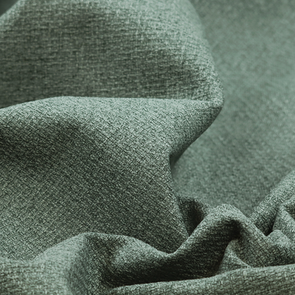 An upholstery fabric in a serene seafoam or muted teal shade. The textile features a dense, multi-tonal weave with interlacing threads of dusty blue-green and dark charcoal, creating a textured, linen-look surface with a matte finish.