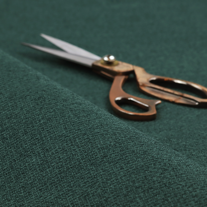 An upholstery fabric in a deep forest or emerald green shade. The textile features a dense, multi-tonal weave with interlaced threads of dark teal and charcoal, creating a rich, textured linen-look surface with a sophisticated matte finish.