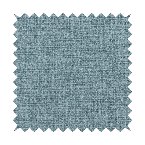 An upholstery fabric in a soft slate blue or dusty denim shade. The textile features a dense, multi-tonal basket weave with interlaced threads of sky blue, muted grey, and charcoal, creating a textured, linen-look surface with a matte finish.