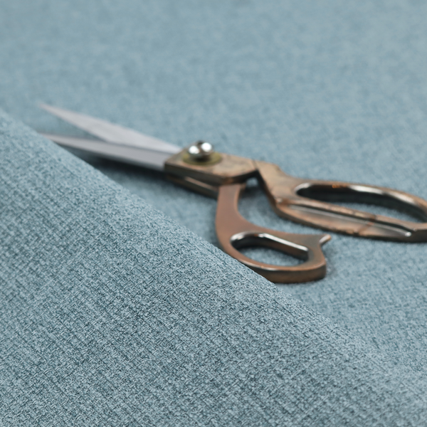 An upholstery fabric in a soft slate blue or dusty denim shade. The textile features a dense, multi-tonal basket weave with interlaced threads of sky blue, muted grey, and charcoal, creating a textured, linen-look surface with a matte finish.