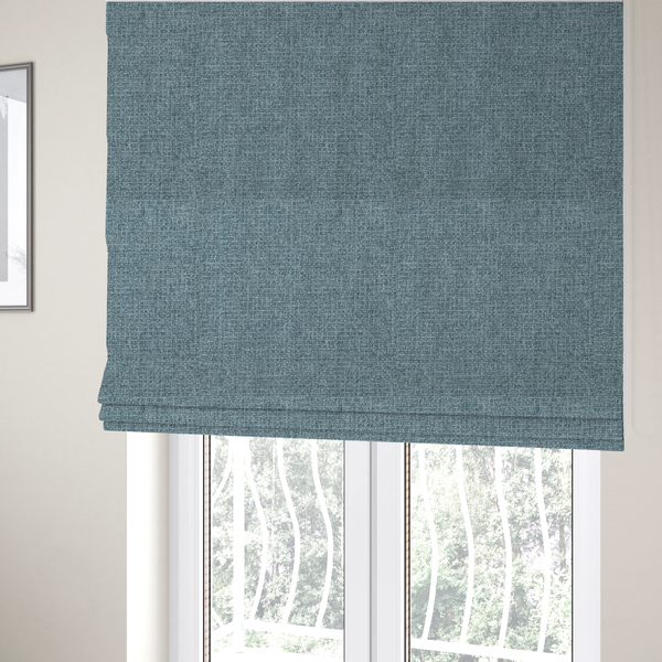 The fabric used to create these Roman blinds is a upholstery fabric in a soft slate blue or dusty denim shade. The textile features a dense, multi-tonal basket weave with interlaced threads of sky blue, muted grey, and charcoal, creating a textured, linen-look surface with a matte finish.