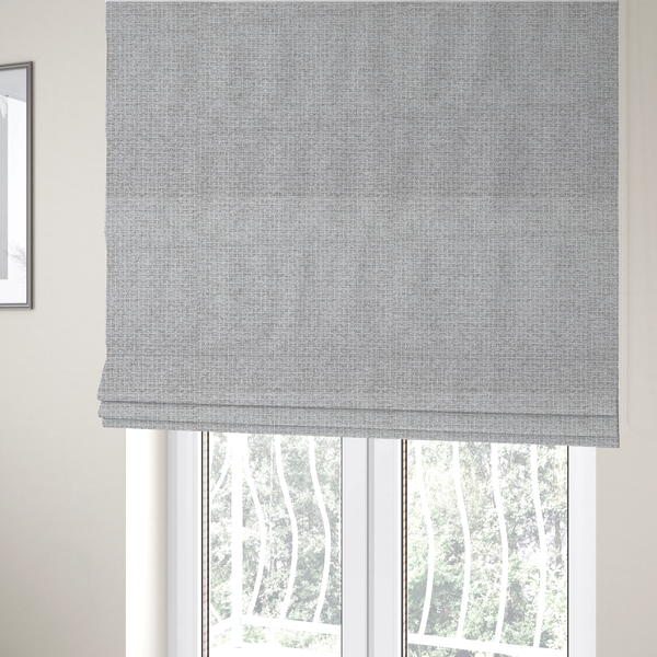 The fabric used to create these Roman blinds is a fabric in a cool-toned light silver or pale grey. The weave features interlaced white and soft grey threads, creating a bright, contemporary textured finish.