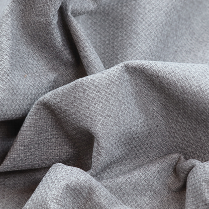 An upholstery fabric in a cool pebble grey. The interlacing of light grey and off-white threads creates a clean, contemporary basket weave pattern with a matte finish.