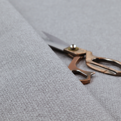 An upholstery fabric in a cool pebble grey. The interlacing of light grey and off-white threads creates a clean, contemporary basket weave pattern with a matte finish.