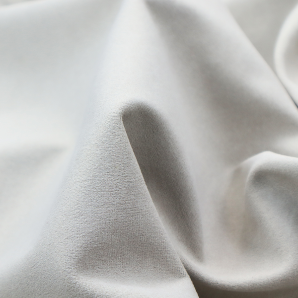 A creamy off-white fabric with a dense, velvety or short-pile texture. The surface is uniform and soft, featuring a fine, grainy appearance that suggests a plush material like micro-suede or high-end upholstery velvet.