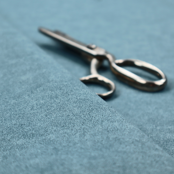 a dusty blue or slate blue fabric with a dense, distressed felt-like texture. The material features a sophisticated mottled pattern of medium blue and muted grey fibres. It contains the signature irregular, light-coloured "crackle" veins characteristic of this collection, giving it the weathered appearance of premium distressed suede or industrial wool.