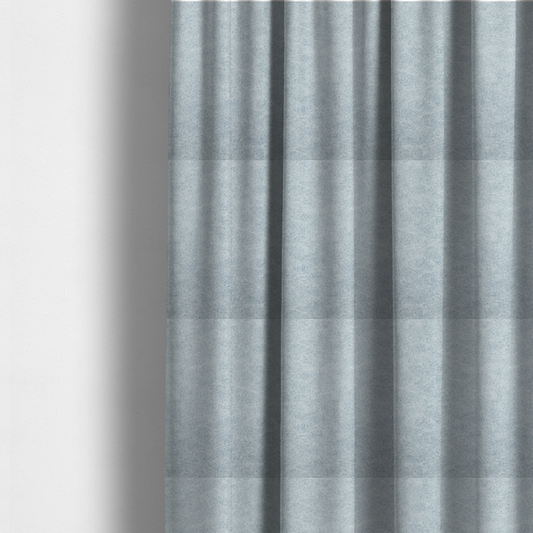 The fabric used to create these made-to-measure curtains is a light sky blue or powder blue fabric with a dense, distressed felt-like texture. The surface features a soft, mottled blend of pale blue and white fibres, creating a subtle weathered effect. It includes the signature irregular, light-coloured "crackle" lines seen throughout this collection, giving it the appearance of weathered microfiber or industrial wool.