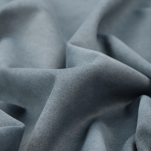 A denim or dusty blue fabric with a dense, distressed felt-like texture. The surface features an intricate mottled blend of slate blue and muted grey fibres. Like the others in this collection, it is defined by organic, light-coloured "crackle" lines and a stippled appearance that mimics the look of weathered suede or high-end industrial wool.