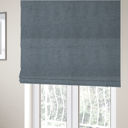 The fabric used to create these Roman blinds is a denim or dusty blue fabric with a dense, distressed felt-like texture. The surface features an intricate mottled blend of slate blue and muted grey fibres. Like the others in this collection, it is defined by organic, light-coloured "crackle" lines and a stippled appearance that mimics the look of weathered suede or high-end industrial wool.