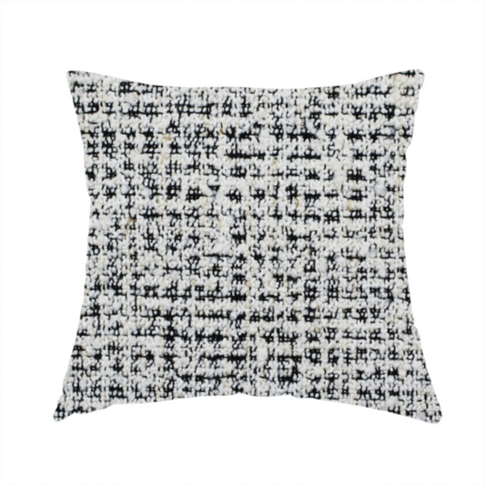 The fabric used to create this handmade cushion is a dense textile with a complex, gridded texture. The fabric is composed of thick white and black yarns interwoven to create a "static" or pixelated marl effect. The weave is highly tactile, showing visible loops, knots, and characteristic of bouclé or tweed. While the overall appearance is monochromatic grey from a distance, the close-up reveals distinct, irregular blocks of stark white and deep black thread.