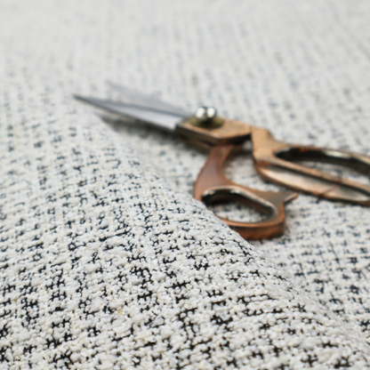 A dense textile with a complex, gridded texture. The fabric is composed of thick white and black yarns interwoven to create a "static" or pixelated marl effect. The weave is highly tactile, showing visible loops, knots, and characteristic of bouclé or tweed. While the overall appearance is monochromatic grey from a distance, the close-up reveals distinct, irregular blocks of stark white and deep black thread.