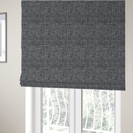 The fabric used to create these Roman blinds is a dark, heavyweight woven fabric with a charcoal and slate-grey salt-and-pepper pattern. The dense bouclé weave creates a highly textured, pebbled surface with subtle off-white specks.