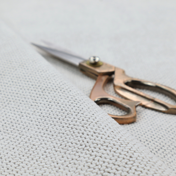 A waffle-knit or honeycomb-patterned weave characterized by a repeating, three-dimensional grid of soft, raised textures. Its off-white or light grey tone and uniform geometric structure suggest a cosy, high-quality material, commonly found in thermal apparel, heavy cotton blankets, or sophisticated upholstery. The dense, woven design provides a matte appearance with a subtle, visually rich depth.