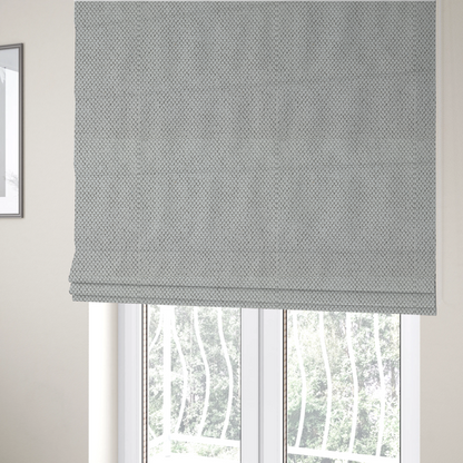 The fabric used to create these Roman blinds is a waffle-knit or honeycomb-patterned weave characterized by a repeating, three-dimensional grid of soft, raised textures. Its off-white or light grey tone and uniform geometric structure suggest a cosy, high-quality material, commonly found in thermal apparel, heavy cotton blankets, or sophisticated upholstery. The dense, woven design provides a matte appearance with a subtle, visually rich depth.