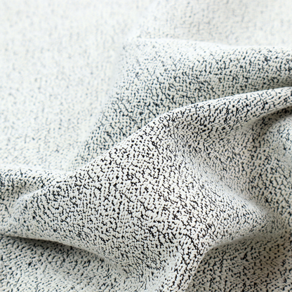 A textured white fabric with an intricate, irregular black speckled pattern throughout.
