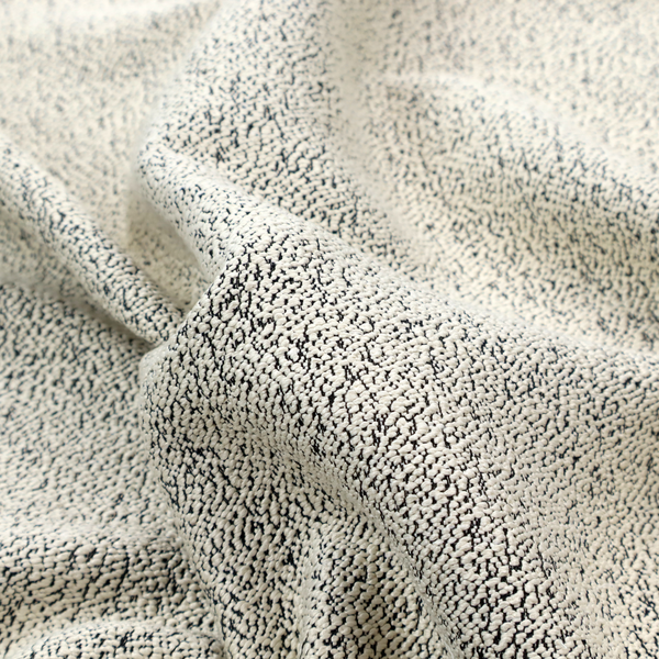 A cream-coloured textured fabric with a dense, irregular black speckled pattern.