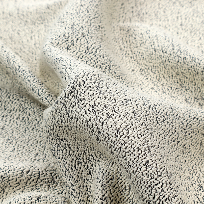 A cream-coloured textured fabric with a dense, irregular black speckled pattern.