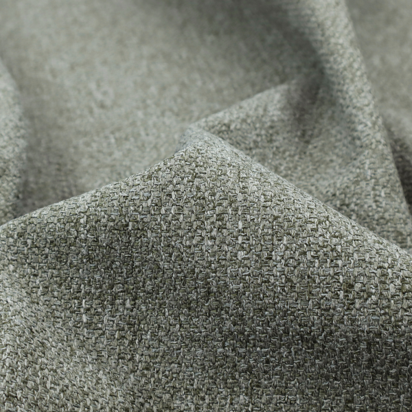 A textured woven upholstery fabric. The material features a dense, multi-tonal weave of sage green, grey, and beige threads, creating a speckled effect with a tactile, matte finish.