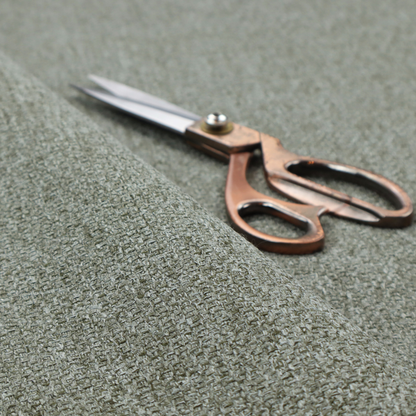 A textured woven upholstery fabric. The material features a dense, multi-tonal weave of sage green, grey, and beige threads, creating a speckled effect with a tactile, matte finish.