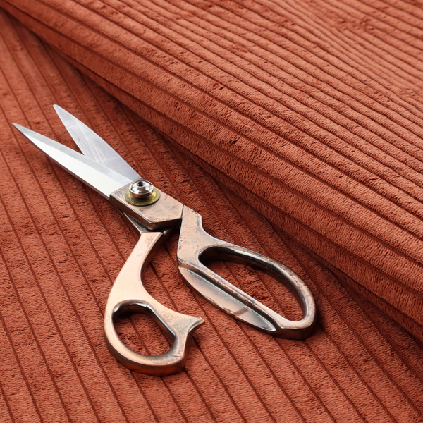 This fabric is a terracotta or burnt orange corduroy featuring a consistent vertical ribbed texture.