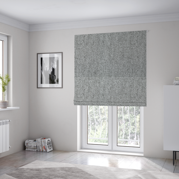 The fabric used to create these Roman blinds is a tight, woven texture with a neutral, monochromatic colour palette. The surface consists of a blend of light grey, charcoal, and white yarns interlocked in a repeating, small-scale geometric pattern.