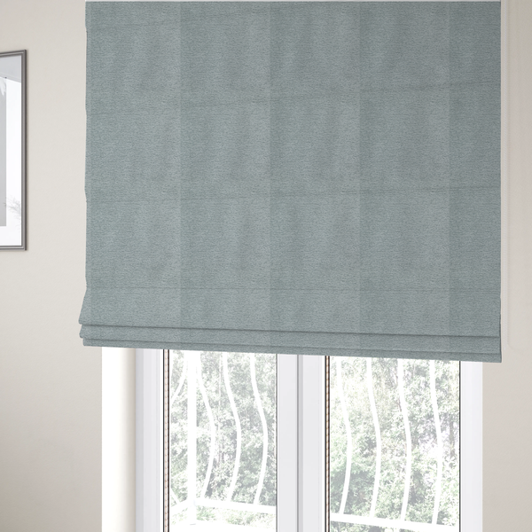 The fabric used to create these Roman blinds is a sophisticated, cool-toned sage green weave with a refined, textured finish. It is crafted with a dense, nubby construction that creates a subtle horizontal ribbing effect, providing both visual dimension and a soft, inviting tactile quality.