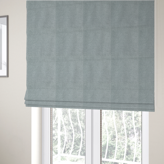 The fabric used to create these Roman blinds is a sophisticated, cool-toned sage green weave with a refined, textured finish. It is crafted with a dense, nubby construction that creates a subtle horizontal ribbing effect, providing both visual dimension and a soft, inviting tactile quality.